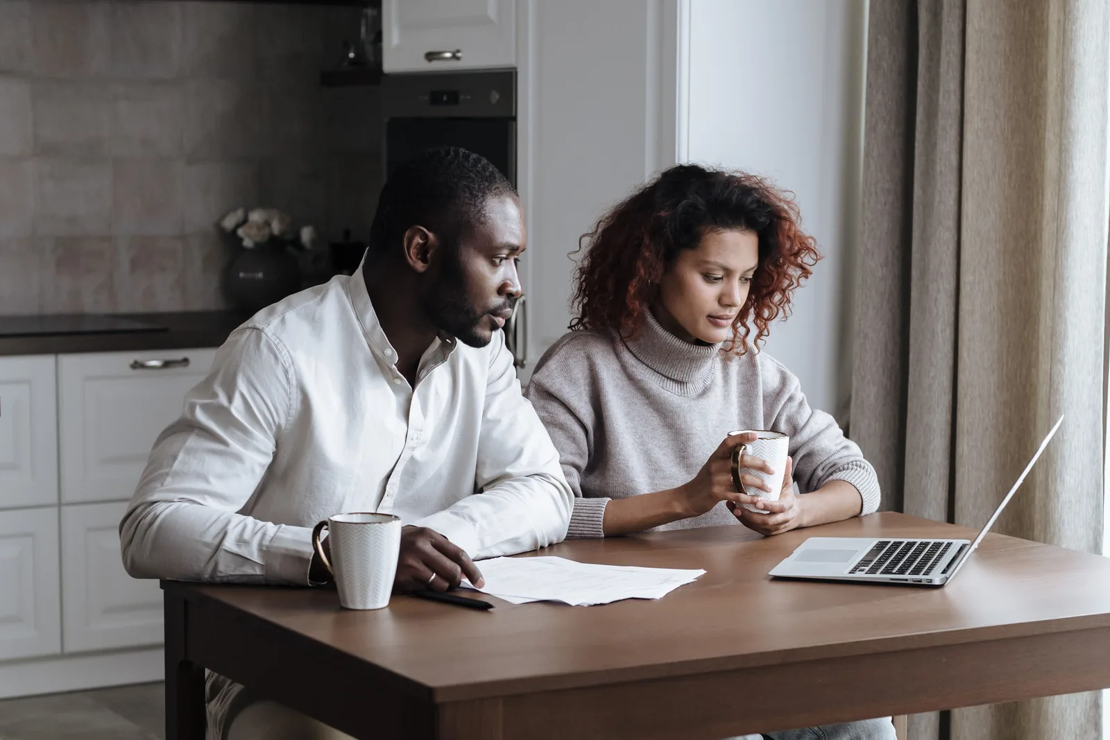 Couple sitting at a kitchen table looking at a laptop together