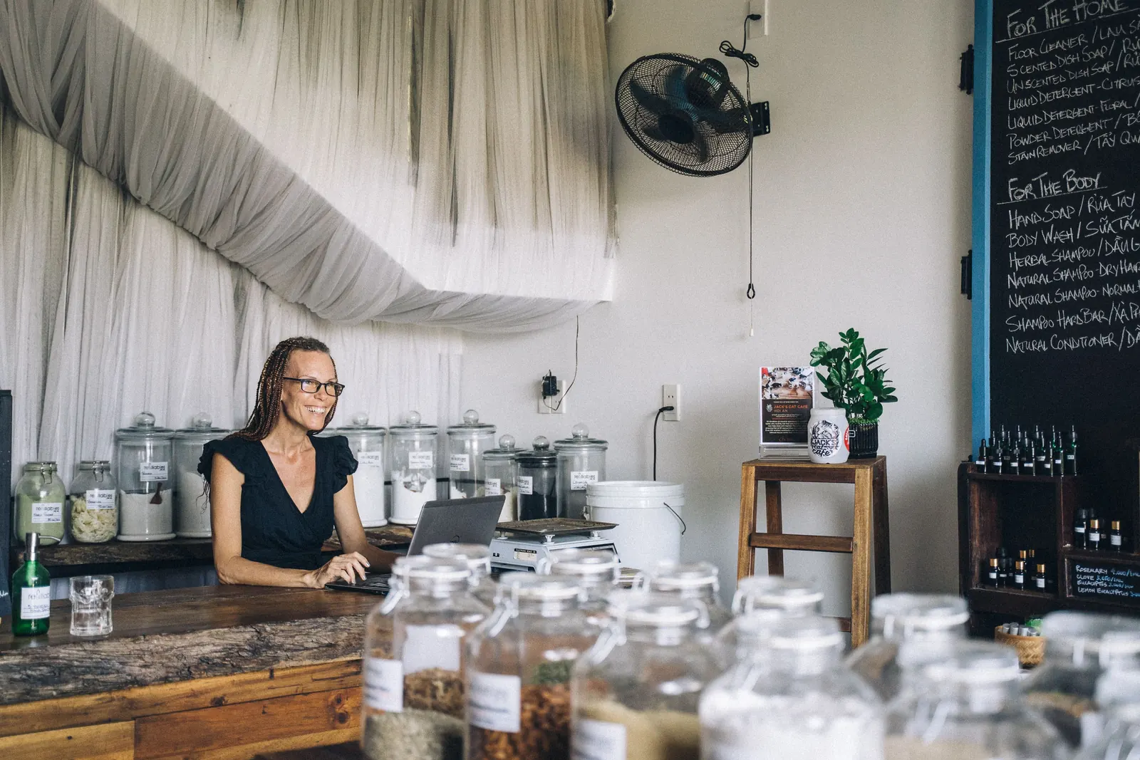 Shop owner smiling at her laptop behind the counter of a small store